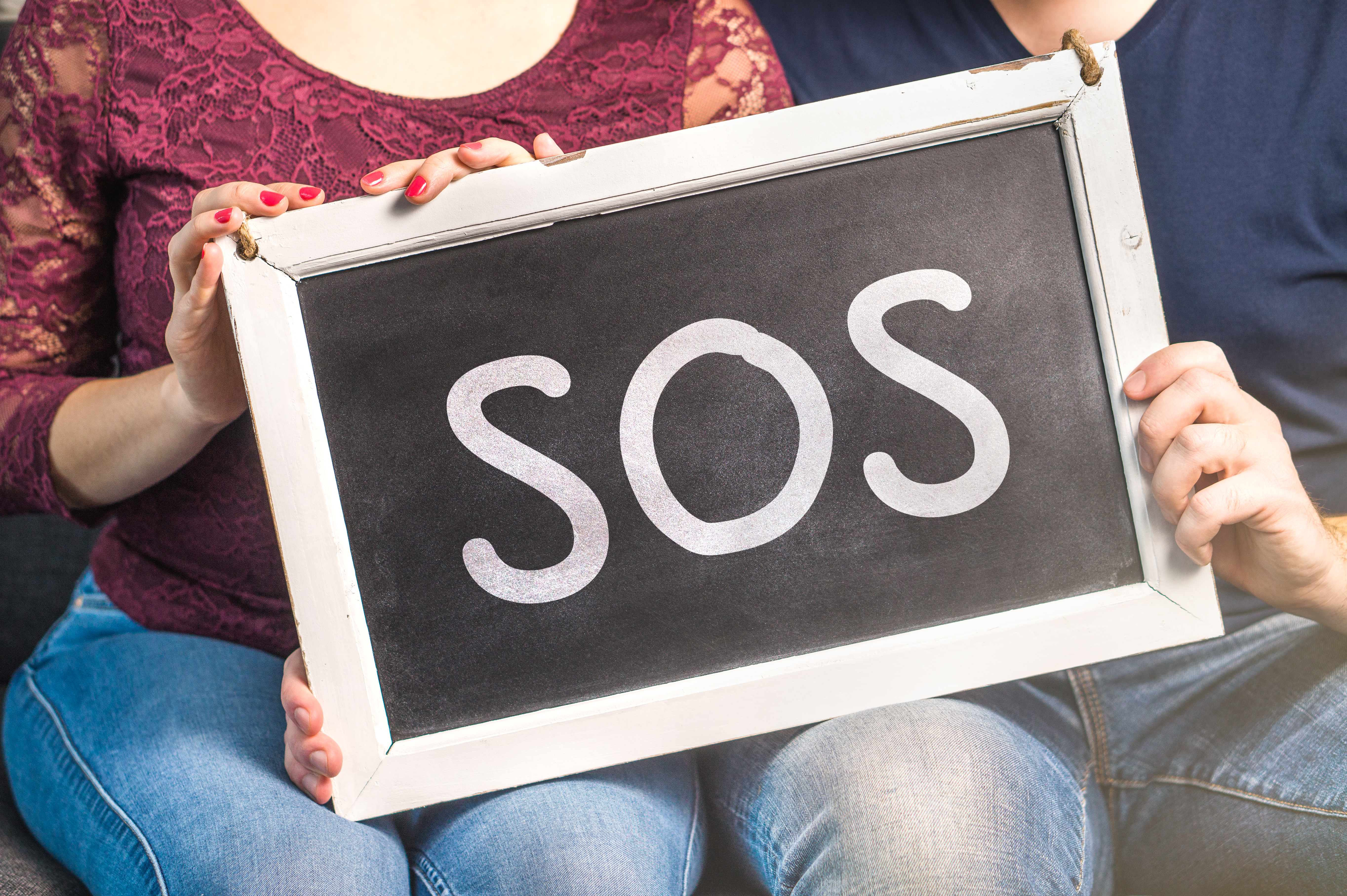 Couples therapy or marriage counseling concept. Needs help for relationship problems. Man and woman holding blackboard with SOS text.